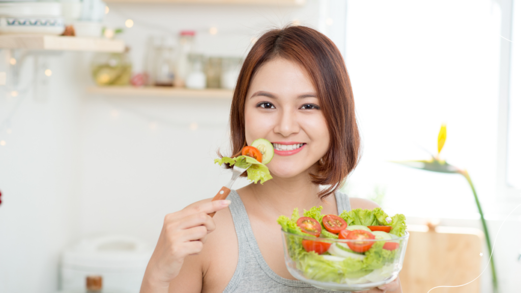 Mulher sorrindo e segurando uma tigela de salada, com uma mão segurando um garfo com uma folha de alface e tomate.