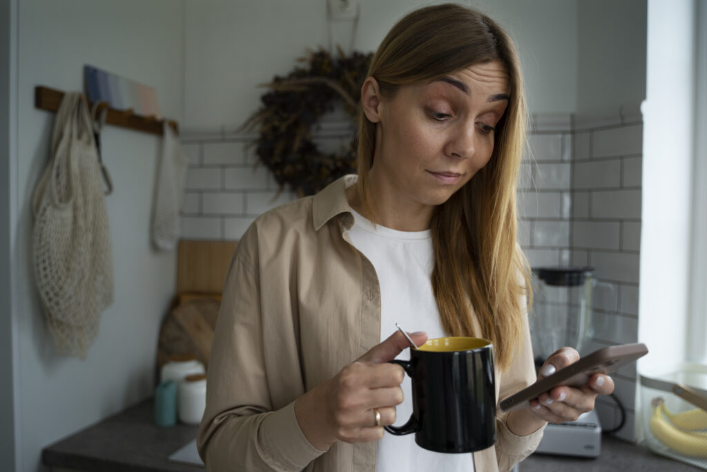 Mulher segurando xícara de chá e celular enquanto reflete sobre estratégias de emagrecimento.