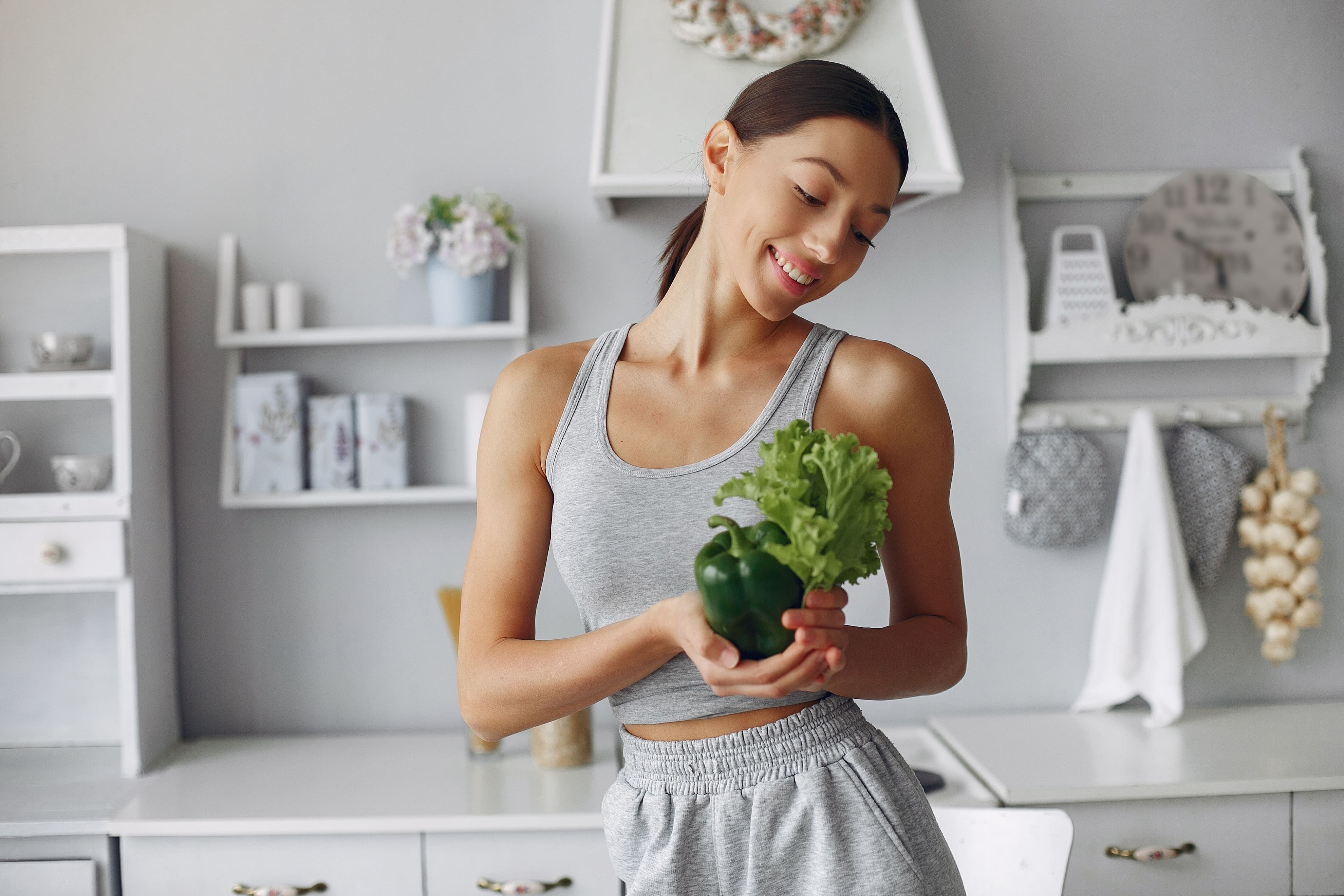 Mulher segurando alface e pimentão verde na cozinha, simbolizando o emagrecimento sustentável com alimentação saudável.