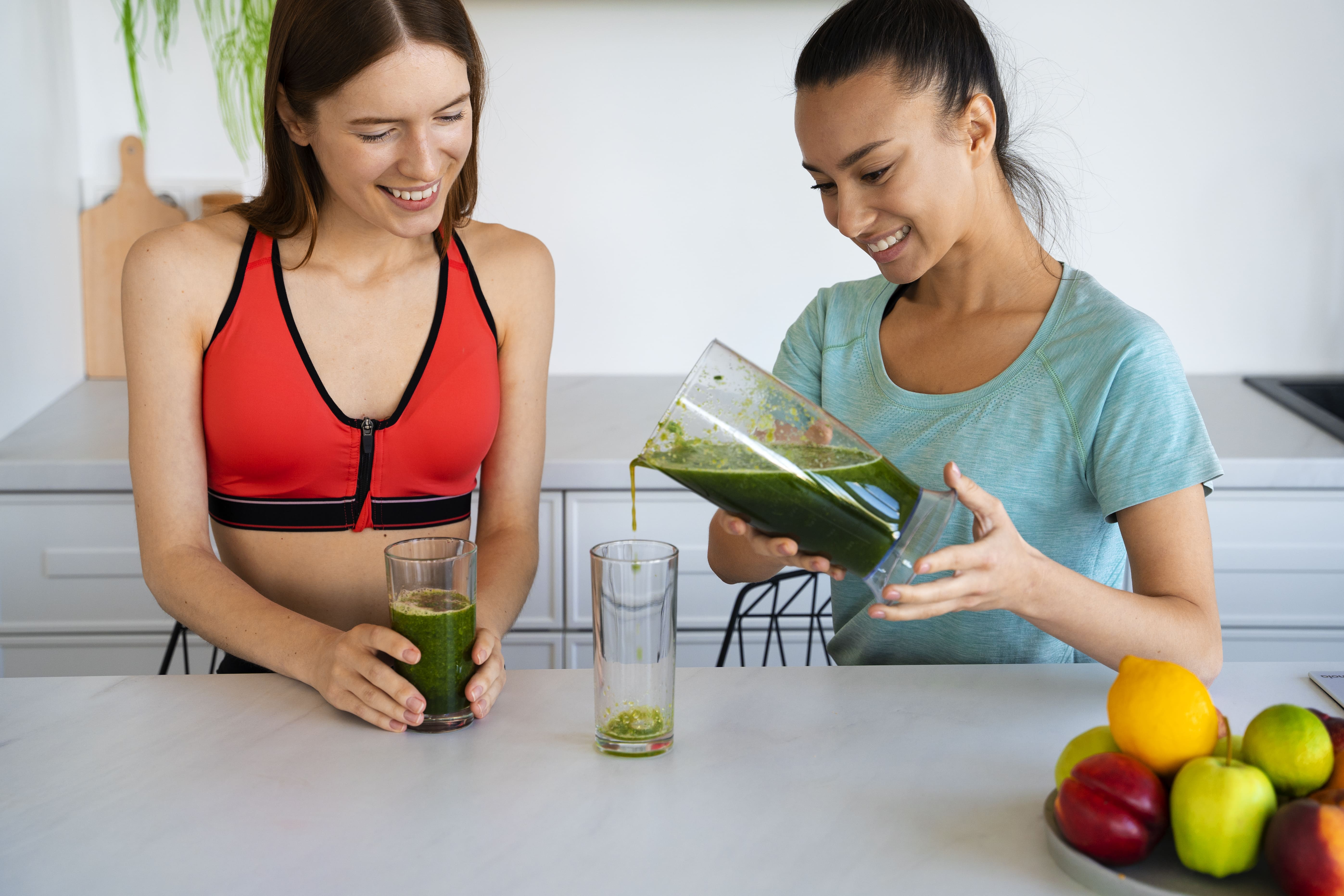 Duas mulheres preparando e bebendo suco verde natural, representando o emagrecimento sustentável com hábitos alimentares saudáveis.