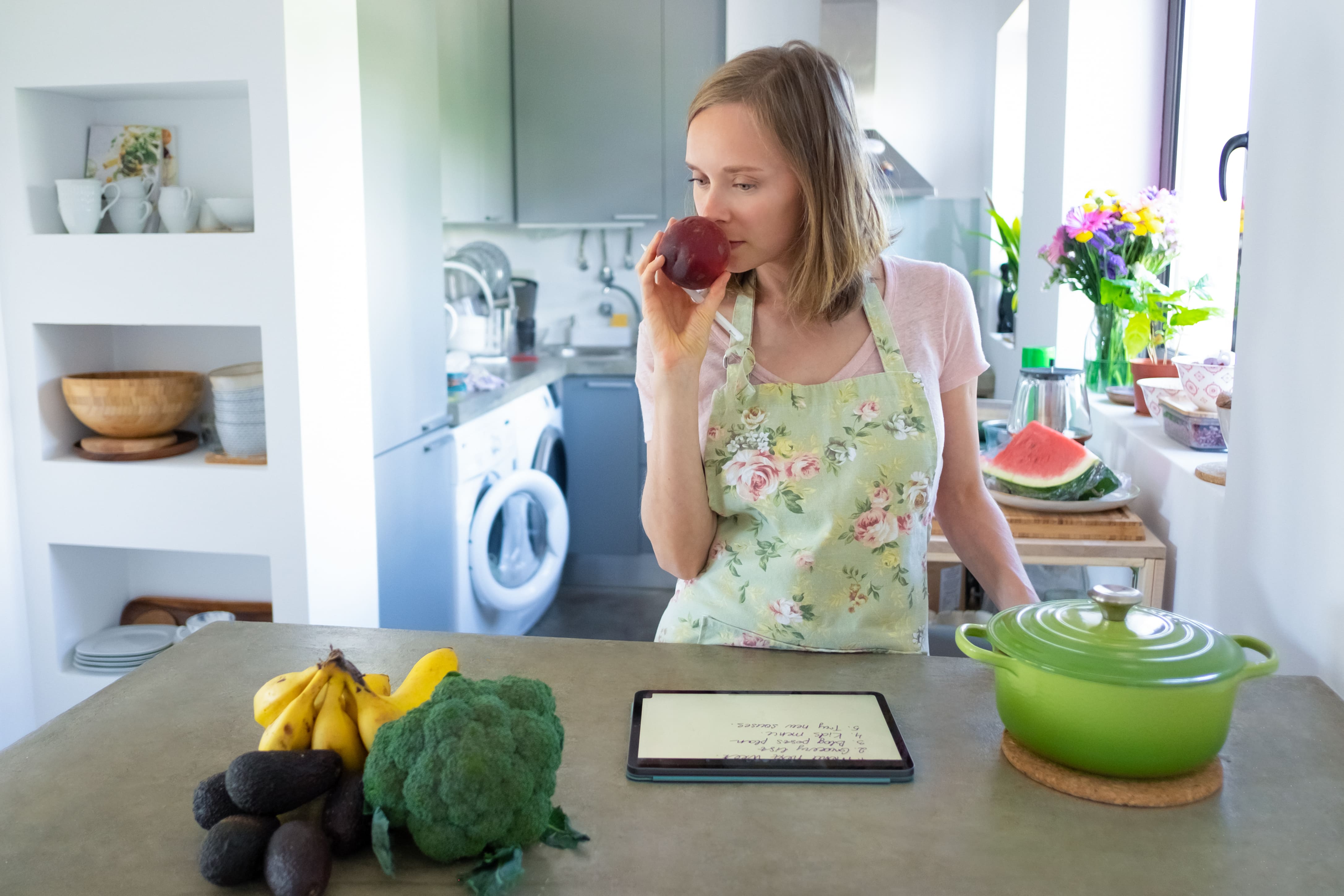Mulher cheirando maçã fresca na cozinha, representando escolhas conscientes para o emagrecimento sustentável.