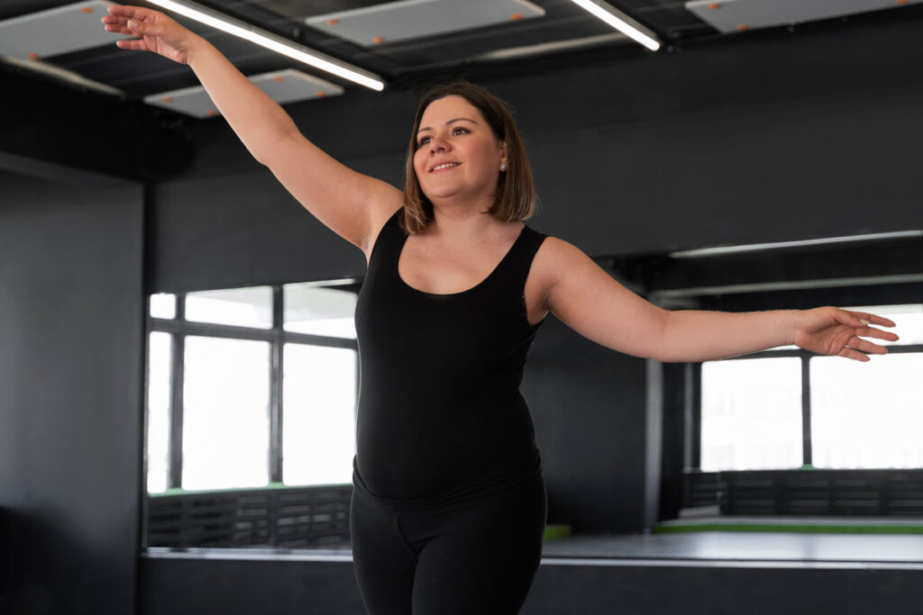 Mulher sorridente praticando dança em estúdio, representando movimento prazeroso e autoestima no processo de emagrecimento.