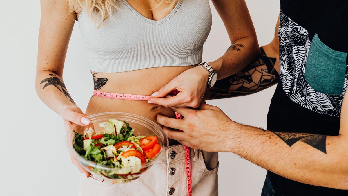 casal segurando tigela de salada e fita métrica simbolizando estilo de vida saudável