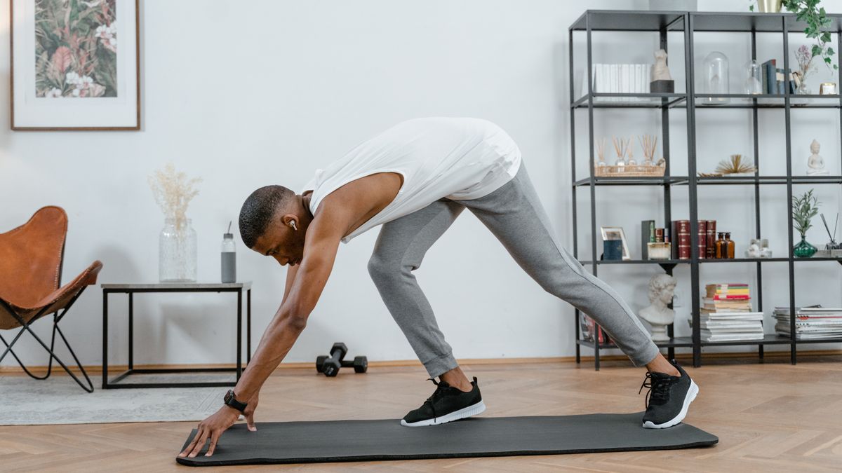 homem fazendo alongamento em tapete de yoga dentro de casa